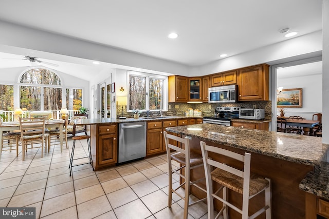 kitchen with brown cabinets, stainless steel appliances, decorative backsplash, a peninsula, and a kitchen bar