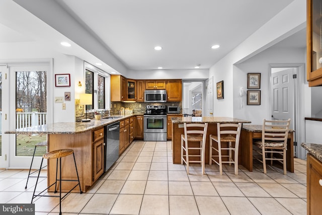 kitchen with a breakfast bar, backsplash, appliances with stainless steel finishes, brown cabinetry, and a peninsula