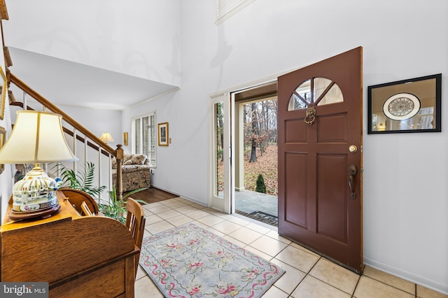 entryway with light tile patterned floors, stairway, a towering ceiling, and baseboards