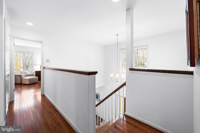 hallway with a chandelier, wood-type flooring, baseboards, and an upstairs landing