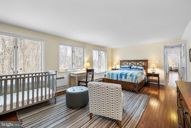 bedroom featuring a baseboard heating unit, a wall mounted AC, hardwood / wood-style flooring, and baseboards