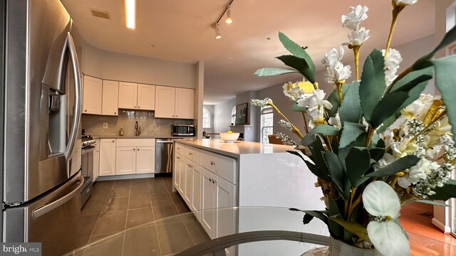 kitchen featuring white cabinets, dark tile patterned floors, stainless steel appliances, and tasteful backsplash