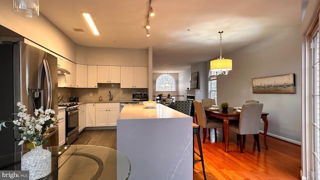 kitchen with stainless steel appliances, pendant lighting, hardwood / wood-style floors, a center island, and white cabinetry