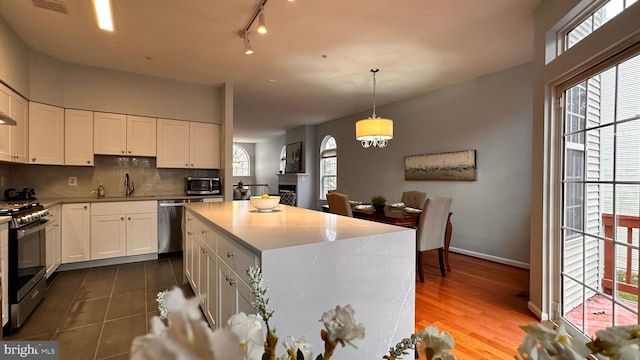 kitchen with decorative light fixtures, stainless steel appliances, white cabinetry, and a healthy amount of sunlight