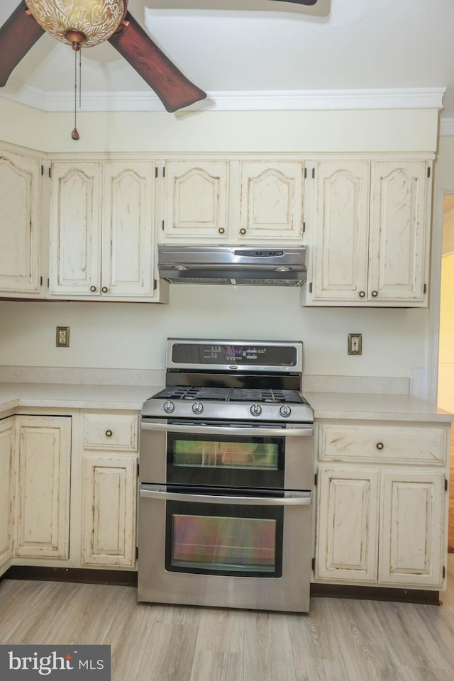 kitchen featuring stainless steel range with gas cooktop, cream cabinets, ornamental molding, and light wood-type flooring