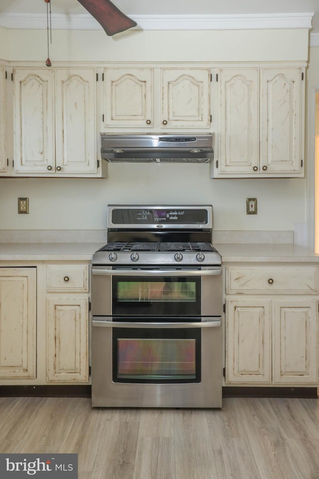 kitchen featuring gas stove, crown molding, light hardwood / wood-style floors, and range hood