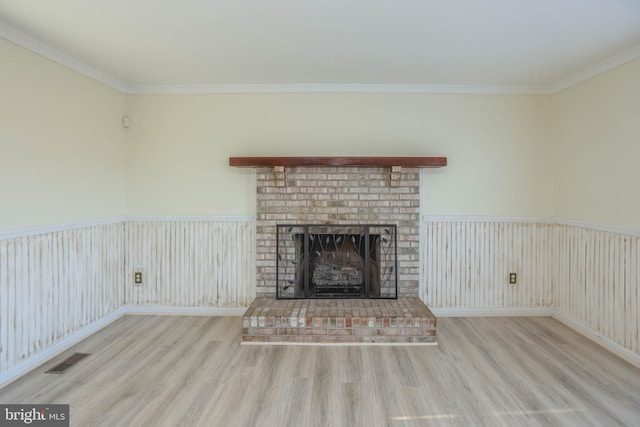 unfurnished living room with a brick fireplace, ornamental molding, and light wood-type flooring