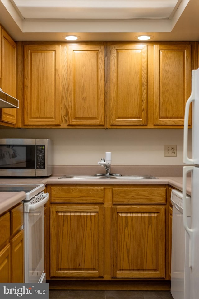 kitchen with a raised ceiling, white appliances, and sink