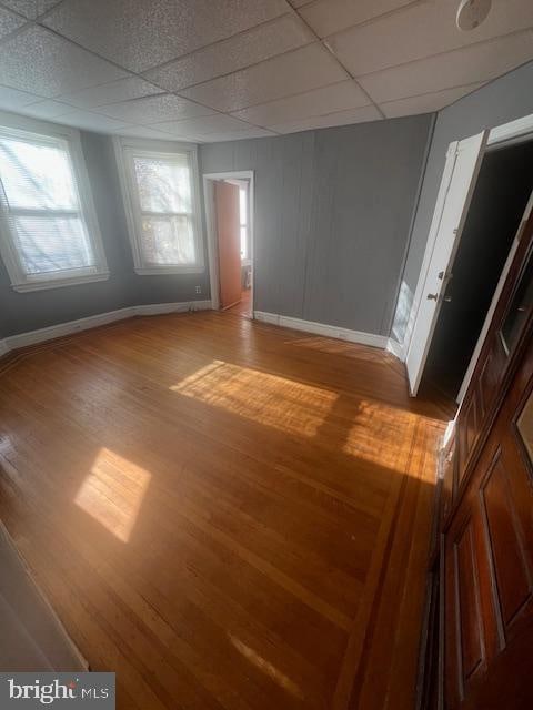 empty room featuring wood-type flooring, a wealth of natural light, and a drop ceiling