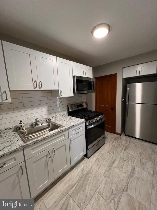 kitchen with light stone countertops, appliances with stainless steel finishes, tasteful backsplash, sink, and white cabinets