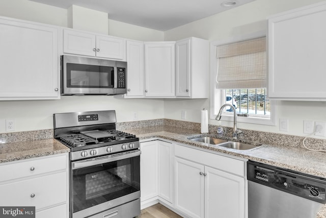 kitchen featuring light stone countertops, appliances with stainless steel finishes, sink, white cabinets, and light hardwood / wood-style floors