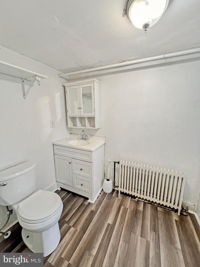 bathroom with wood-type flooring, vanity, toilet, and radiator