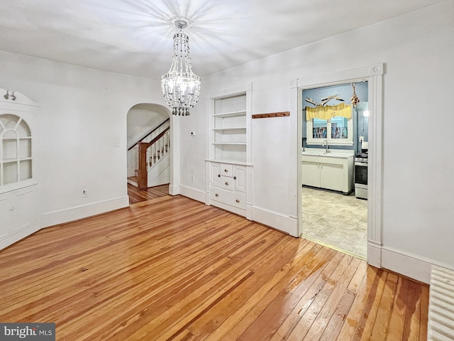 unfurnished dining area featuring a chandelier, built in features, wood-type flooring, and sink