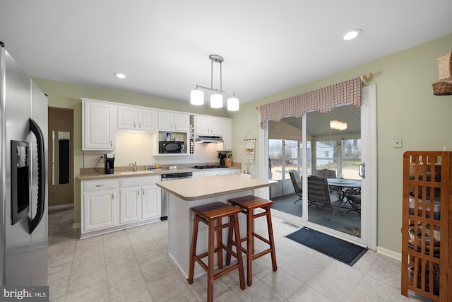 kitchen featuring a center island, hanging light fixtures, appliances with stainless steel finishes, a kitchen breakfast bar, and white cabinets