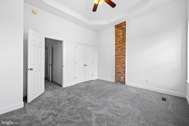 unfurnished bedroom featuring dark colored carpet, a closet, a raised ceiling, and ceiling fan