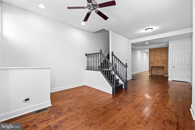 stairs with ceiling fan, hardwood / wood-style floors, and a brick fireplace