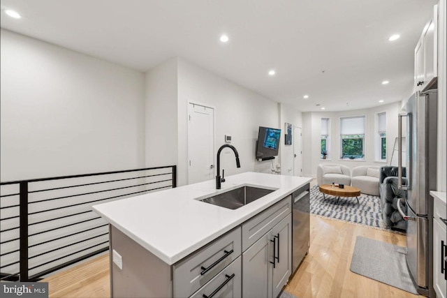 kitchen with appliances with stainless steel finishes, light wood-type flooring, gray cabinetry, sink, and a center island with sink