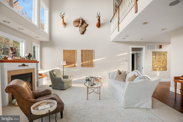 living area featuring a high ceiling, visible vents, wood finished floors, and a glass covered fireplace