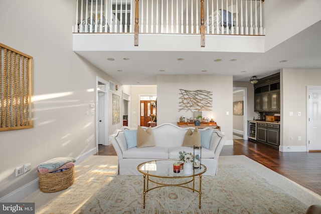 living area featuring a towering ceiling, beverage cooler, baseboards, and dark wood-type flooring