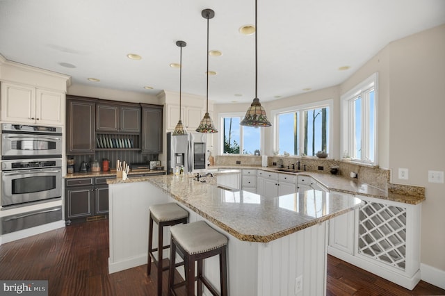 kitchen with dark wood-style flooring, a warming drawer, appliances with stainless steel finishes, a sink, and a kitchen island