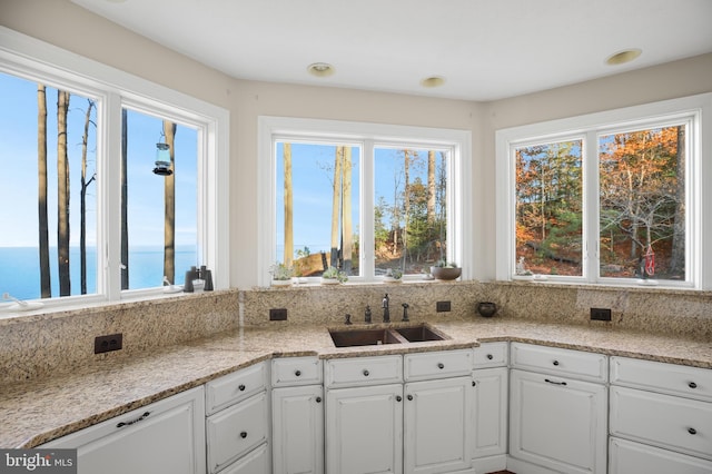 kitchen with light stone counters, a water view, a sink, and white cabinetry