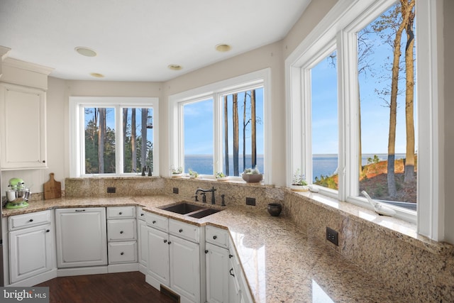 kitchen with dark wood finished floors, light stone counters, a water view, white cabinetry, and a sink