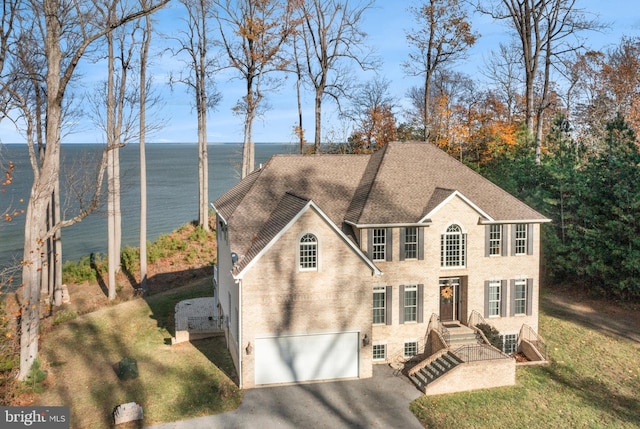 view of front facade featuring a garage, a shingled roof, aphalt driveway, a water view, and brick siding