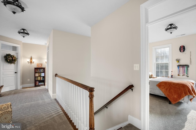 hallway with visible vents, carpet floors, an upstairs landing, and baseboards