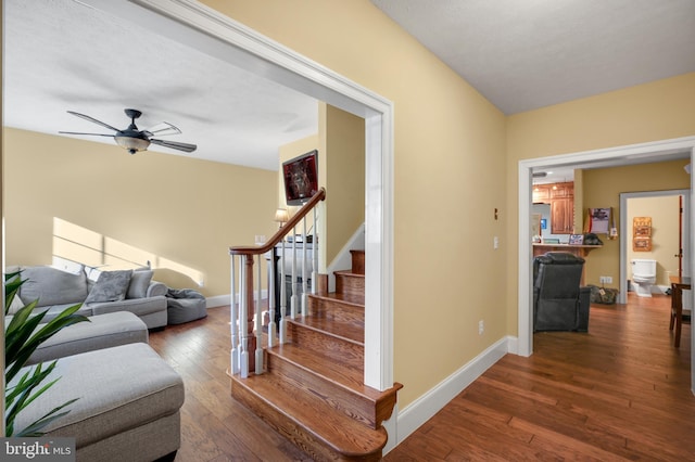 stairs with hardwood / wood-style floors, a ceiling fan, and baseboards