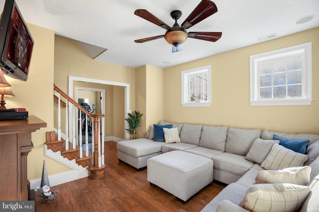 living area with ceiling fan, dark wood-style flooring, visible vents, baseboards, and stairway