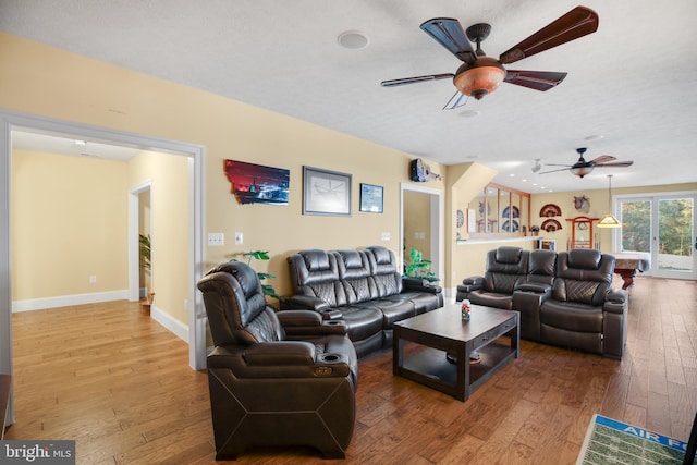 living room with a textured ceiling, wood-type flooring, a ceiling fan, and baseboards