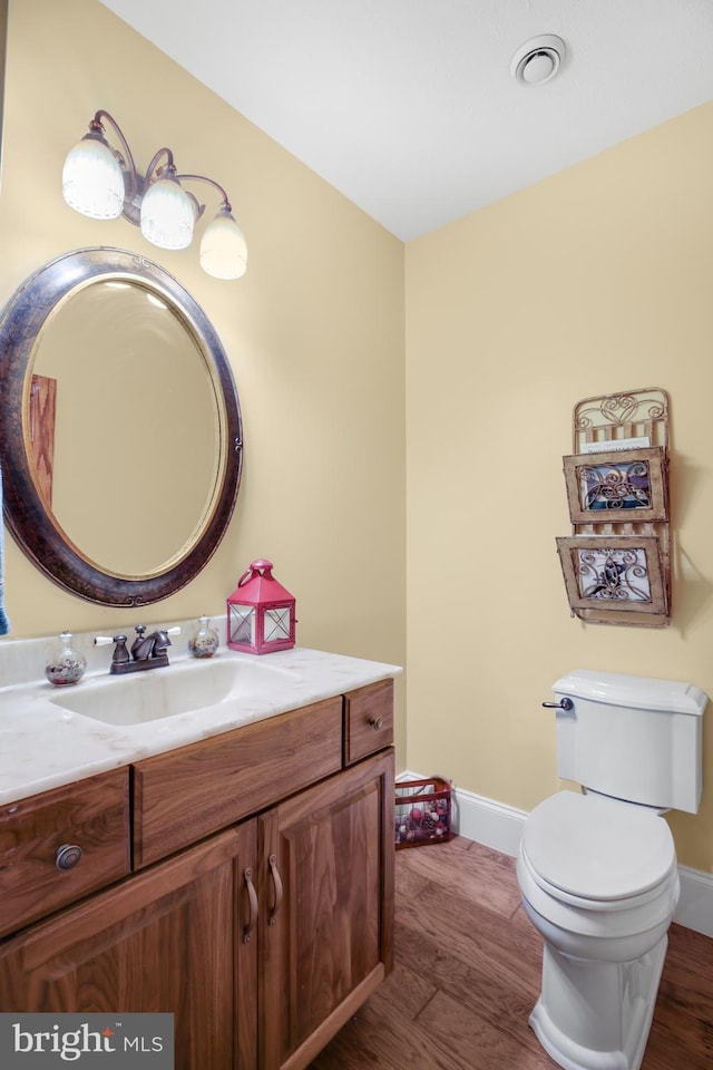 half bathroom with toilet, wood finished floors, vanity, and baseboards