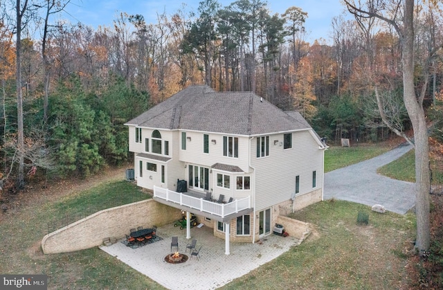 rear view of property featuring driveway, an outdoor fire pit, roof with shingles, a yard, and a patio area