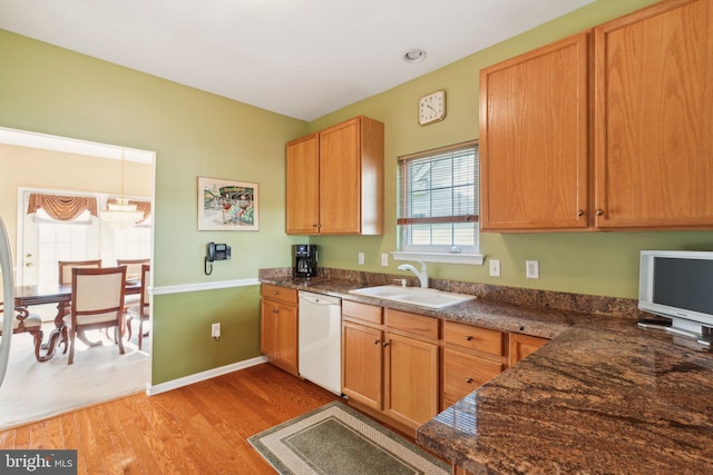 kitchen with white dishwasher, sink, hanging light fixtures, and light hardwood / wood-style flooring