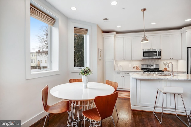 kitchen with light stone counters, hanging light fixtures, appliances with stainless steel finishes, white cabinets, and a sink