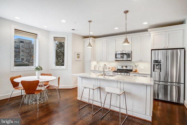 kitchen featuring appliances with stainless steel finishes, hanging light fixtures, a kitchen island with sink, white cabinetry, and a sink