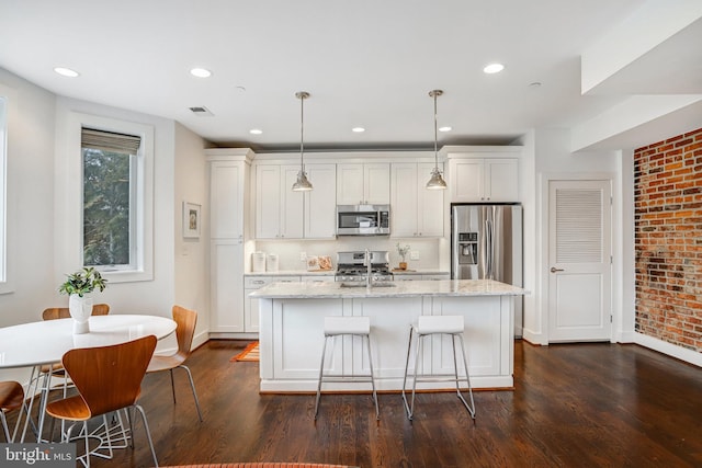 kitchen featuring light stone counters, white cabinets, hanging light fixtures, appliances with stainless steel finishes, and dark wood-style floors