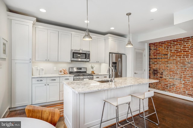 kitchen with decorative light fixtures, stainless steel appliances, a sink, white cabinetry, and a center island with sink