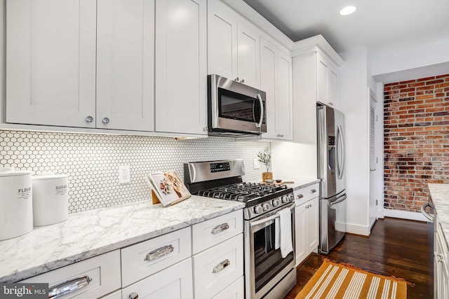 kitchen featuring light stone counters, brick wall, dark wood-type flooring, white cabinetry, and appliances with stainless steel finishes