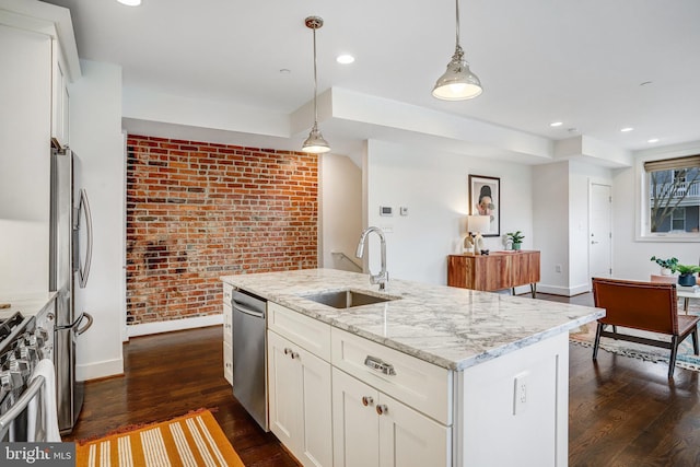 kitchen featuring a kitchen island with sink, a sink, appliances with stainless steel finishes, light stone countertops, and decorative light fixtures