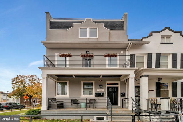 view of property featuring covered porch, fence, a balcony, and stucco siding