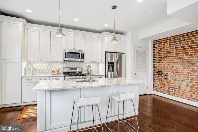 kitchen with stainless steel appliances, a sink, a center island with sink, and white cabinets