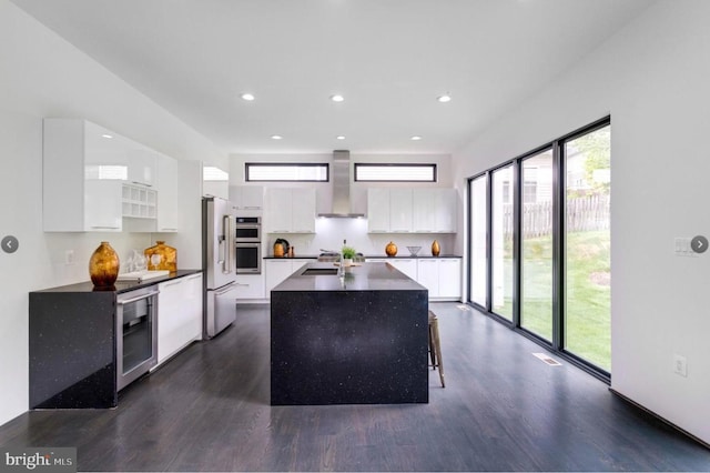 kitchen with dark hardwood / wood-style flooring, stainless steel appliances, wall chimney range hood, white cabinets, and a center island