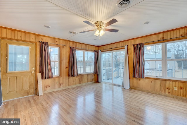 interior space with light hardwood / wood-style floors, ceiling fan, crown molding, and wood walls