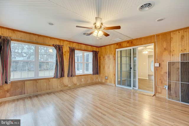 spare room featuring ornamental molding, light wood-type flooring, a wealth of natural light, and wooden walls