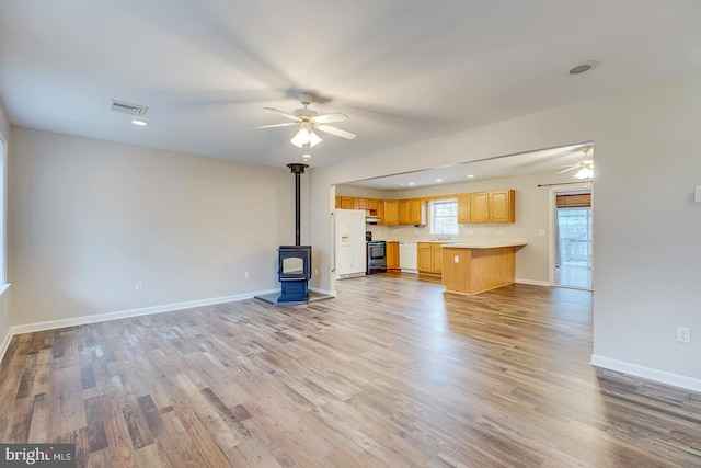 unfurnished living room featuring a wood stove, light hardwood / wood-style flooring, and ceiling fan