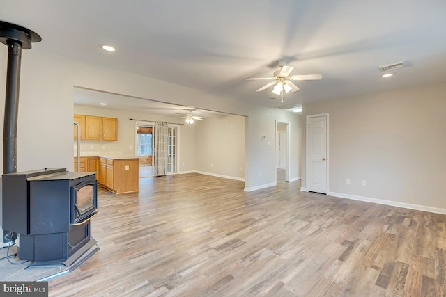 living room featuring a wood stove, light hardwood / wood-style flooring, and ceiling fan