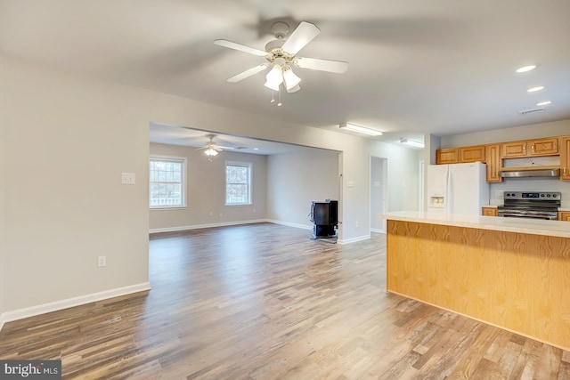 kitchen with a wood stove, electric range, ceiling fan, hardwood / wood-style flooring, and white fridge with ice dispenser