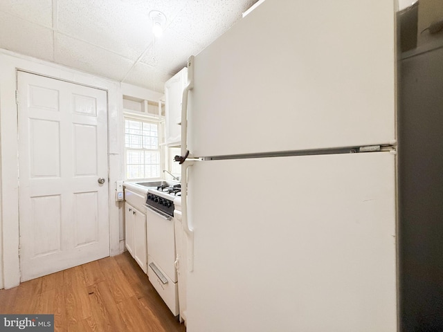 kitchen with white cabinets, white appliances, and light hardwood / wood-style floors