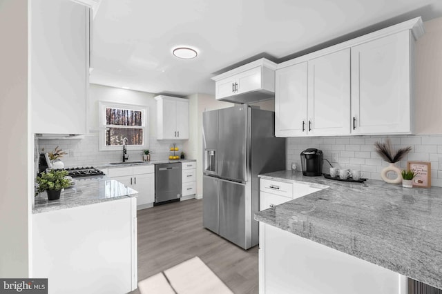 kitchen with light stone countertops, light wood-type flooring, stainless steel appliances, sink, and white cabinets